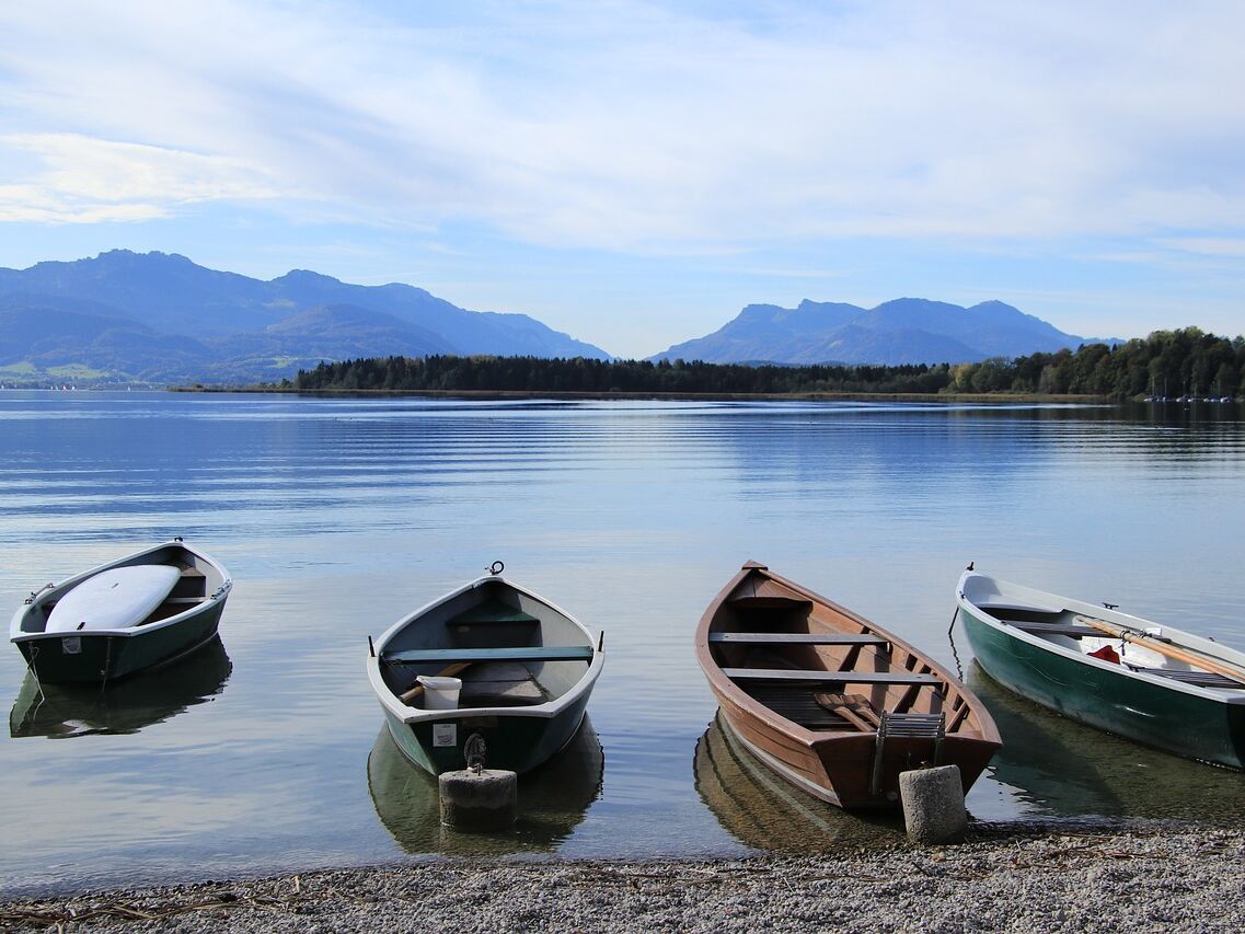 Blick auf den Chiemsee an dem vier kleine Boote am Ufer schwimmen