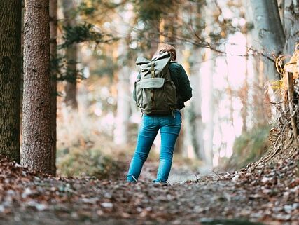 Eine Frau die mit einem Rucksack auf dem Rücken auf einem Waldweg steht und sich verlaufen hat.