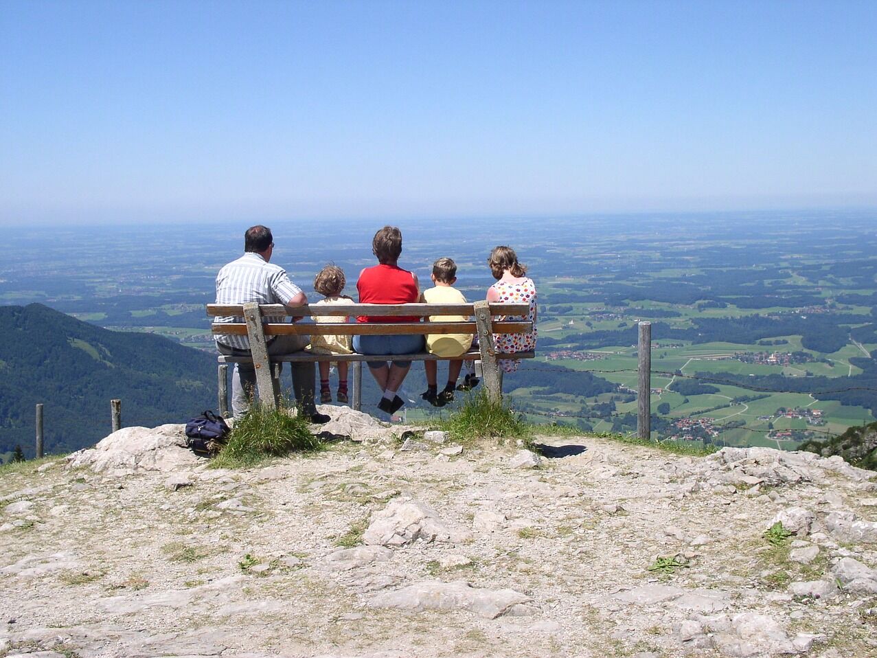 Eine Familie die den Ausblick von der Kampenwand aus, auf einer Bank genießt