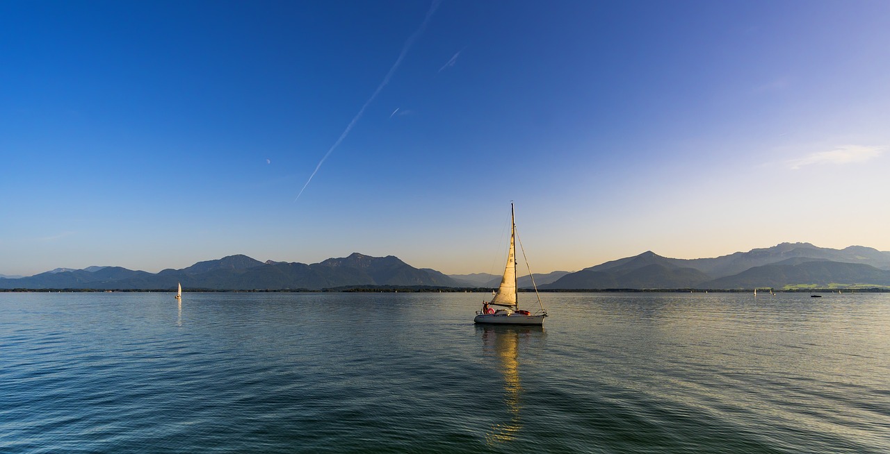 Blick auf den Chiemsee auf dem ein kleines Boot schwimmt, vom Ufer aus