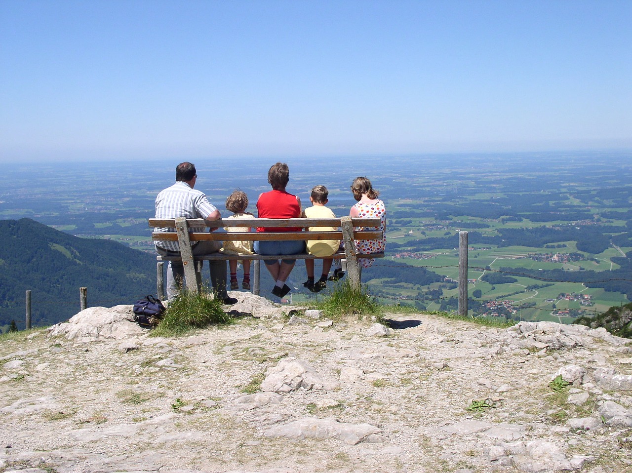 Eine Familie die den Ausblick von der Kampenwand aus, auf einer Bank genießt